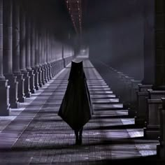 a person in a hooded cloak walking down a dark hallway with columns on either side