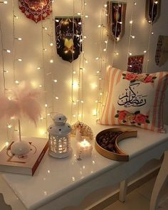 a white table topped with lots of pillows and lights next to a wall covered in pictures