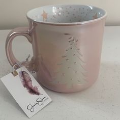 a pink coffee mug with a christmas tree on it and a tag hanging from the handle