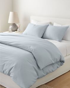 a bed with blue sheets and pillows on top of it in a bedroom next to a lamp