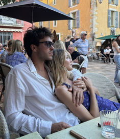 a man sitting next to a woman on top of a chair in front of an umbrella