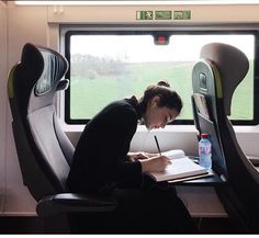 a woman writing on a paper while sitting in a seat next to an open window