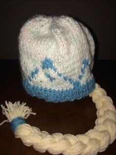 a white and blue knitted hat sitting on top of a wooden table next to a rope