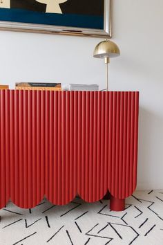 a red cabinet in the corner of a room with a painting on the wall behind it