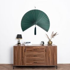 a wooden cabinet with a green fan hanging on it's sideboard next to a lamp