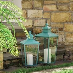 two green lanterns sitting on the side of a stone building next to a planter