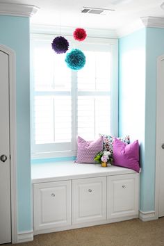 a room with blue walls, white cabinets and colorful pom - poms hanging from the window