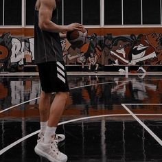 a man standing on top of a basketball court with a ball in his hand and an orange wall behind him