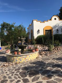 a fountain in front of a house with cactus and rocks around it on a sunny day