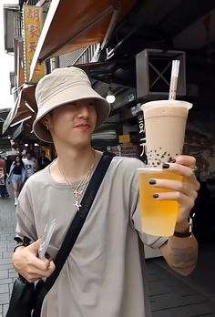 a man holding up a drink in his hand and wearing a hat on the street