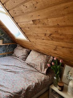 a bed in a bedroom under a slanted roof with flowers on the nightstands