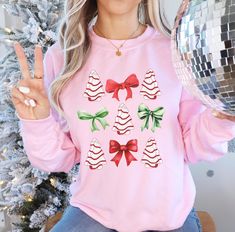 This cute Christmas Sweatshirt is the perfect Christmas Sweatshirt for anyone looking for a trendy holiday sweater! Features Christmas Tree Cakes and Coquette Christmas Bows, and is available in a variety of colors: Pink Christmas, Red Christmas, Green Christmas, and many more!  HOW TO ORDER: 1. Select size 2. Select color 3. Add to cart 4. Repeat steps 1-3 for multiple items 5. Check out PRODUCT INFO: * Gildan 18000 Crewneck * Unisex Sizing * Tear away label * Soft & Stylish * Retail fit PROCES Pink Tops As Winter Gifts, Cute Winter Holiday Tops, Holiday Long Sleeve Tops As Gifts, Holiday Long Sleeve Tops As A Gift, Cute Pink Holiday Tops, Cute Long Sleeve Tops For Festive Occasions, Cute Pink Holiday Top, Cute Pink Top For Holiday, Cute Pink Christmas Tops