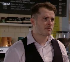 a man in a white shirt and black tie standing in front of a coffee shop