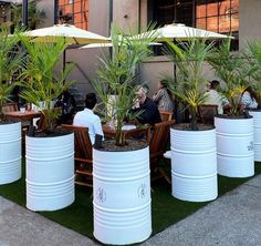 people are sitting at tables with umbrellas and plants in large white containers on the grass