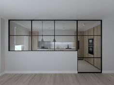 an empty living room with wood floors and glass walls on the wall, looking out onto the kitchen