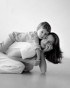 a woman holding a child while laying on the floor in front of a white wall