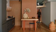 a person standing in a kitchen next to a table with a vase on top of it