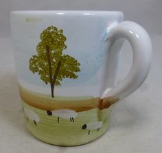 a coffee cup painted with sheep and a tree on it's side, sitting on a table