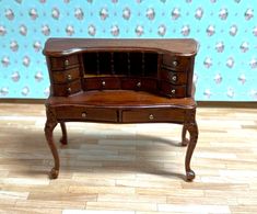 a miniature wooden desk with drawers on the top and bottom, in front of a floral wallpapered background