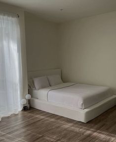 a white bed sitting in the middle of a bedroom next to a window with sheer curtains