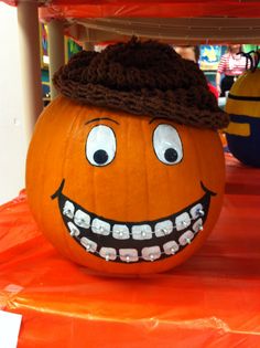 an orange pumpkin with a hat on it's head and teeth painted on the face