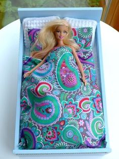 a barbie doll laying in a bed with a colorful blanket on it's back