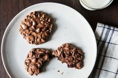 three chocolate cookies on a plate next to a glass of milk