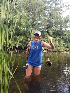 a woman standing in the water while holding a fishing pole and wearing a blue shirt