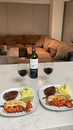 two plates of food and wine on a table in front of a couch with a bottle of wine