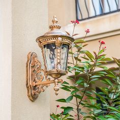 an old fashioned street light on the side of a building with flowers growing in front of it