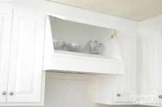 a kitchen with white cupboards and dishes on the shelf above the stove top oven