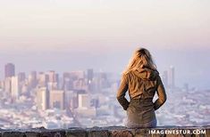 a woman sitting on top of a stone wall looking out over a cityscape