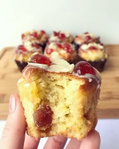 a person holding up a muffin with cherries on top and white frosting