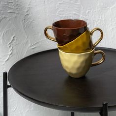 three coffee cups sitting on top of a table next to each other in different colors