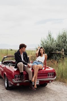 a man and woman sitting on the back of a red car