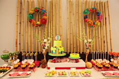 a table topped with lots of food next to bamboo poles and wall hangings filled with wreaths