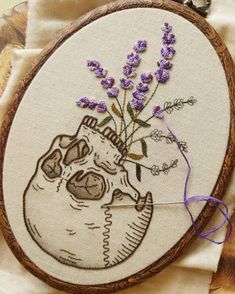 a cross stitch embroidery project with lavenders and a skull holding a flower in it's mouth