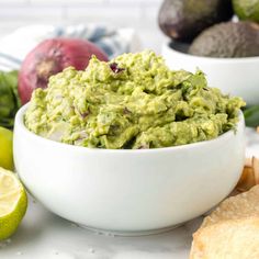 guacamole in a white bowl surrounded by avocados, limes and bread