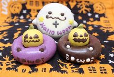 three decorated doughnuts sitting on top of a black and yellow table cloth with halloween decorations