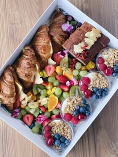 an assortment of fruits and pastries in bowls on a tray with croissants