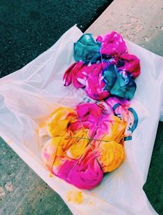 three different colored pieces of cloth sitting on top of a white plastic bag next to a sidewalk