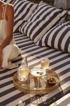 a woman sitting on top of a bed next to a tray filled with drinks