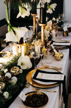 the table is set with black and gold place settings, white flowers, greenery and candles