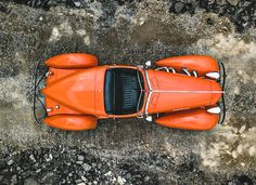 an overhead view of an orange sports car on the ground with rocks and gravel in the background