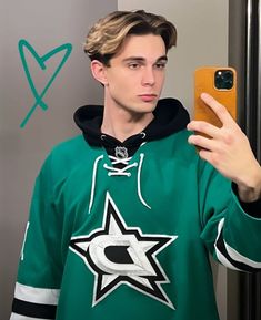 a young man taking a selfie in front of a mirror wearing a green hockey jersey