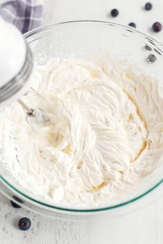 a glass bowl filled with whipped cream and blueberries on top of a white table