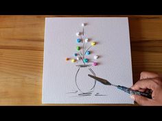 a person is holding a paintbrush and painting a flower in a vase on paper