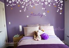 a bedroom with purple walls and white flowers on the headboard, two stuffed animals in front of the bed