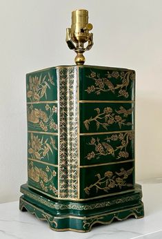 a green and gold decorated chest on top of a white table next to a candle