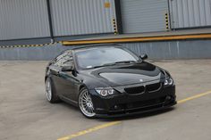 a black sports car parked in front of a warehouse building with yellow lines on the ground